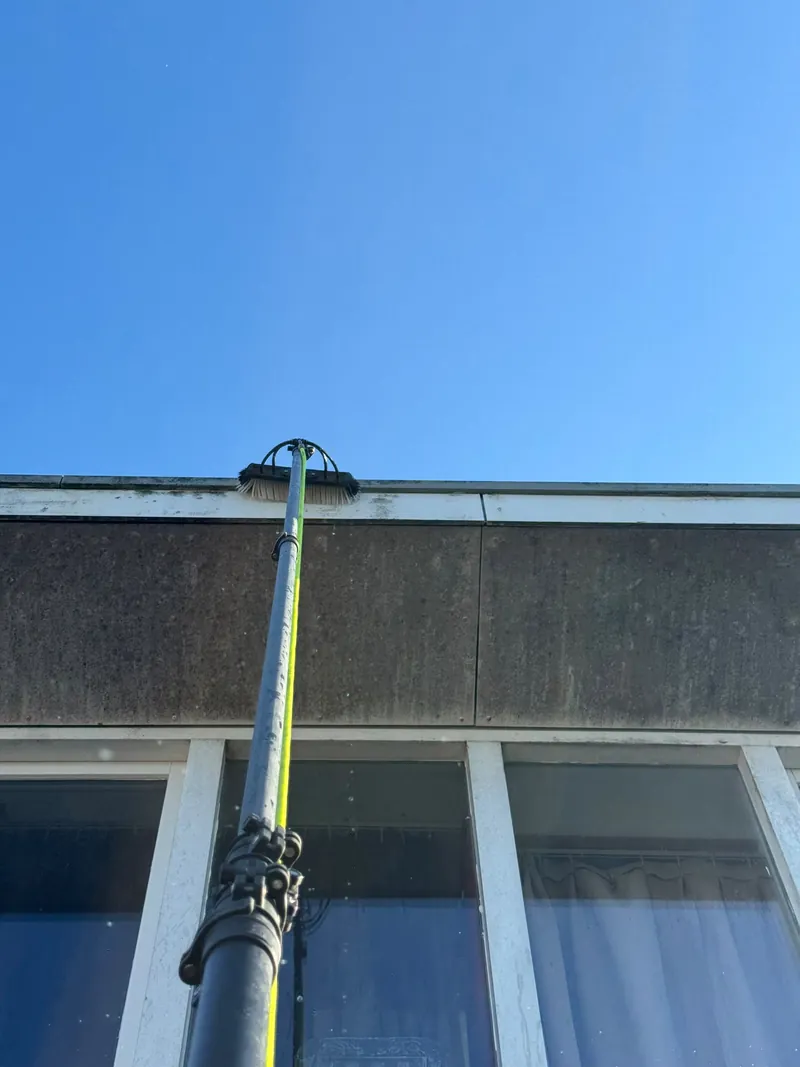 Glazenwasser reinigt de ramen van een dakkapel met een telescoopsteel